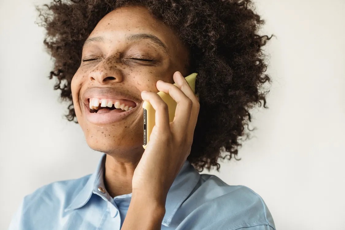 A woman laughing while talking on a yellow phone; illustrative stock photo, not Block or Dessa