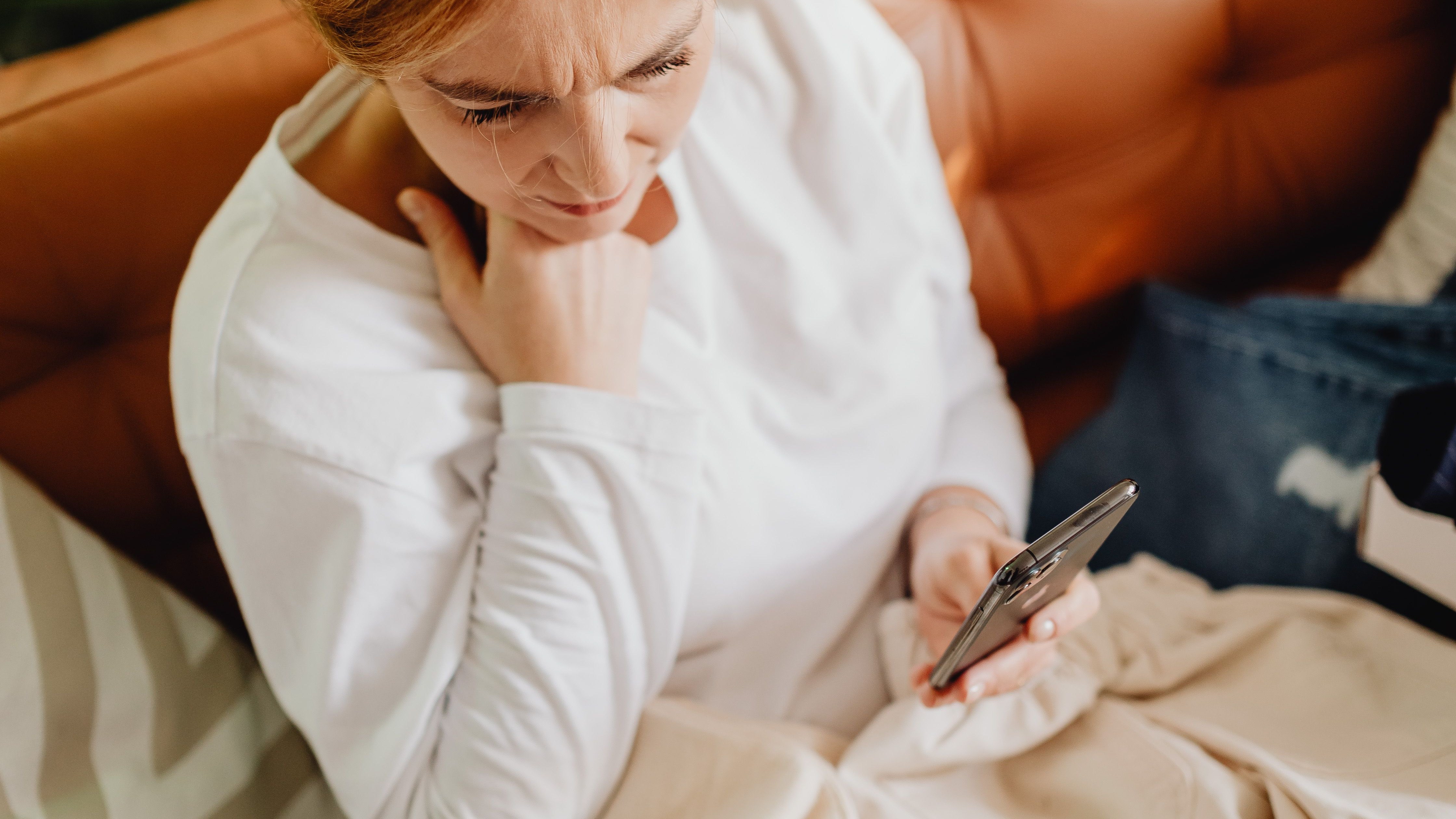 Woman sitting on a sofa looking worried while using her phone