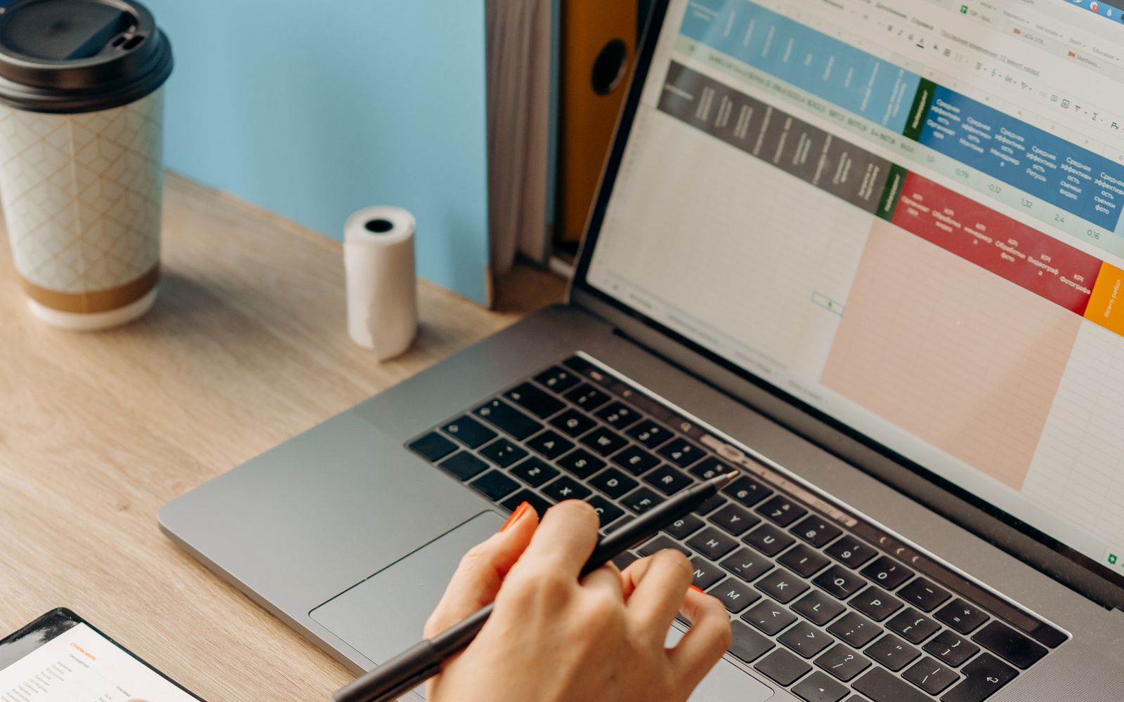 A person working at a laptop with a spreadsheet open on the screen, office binders on the desk