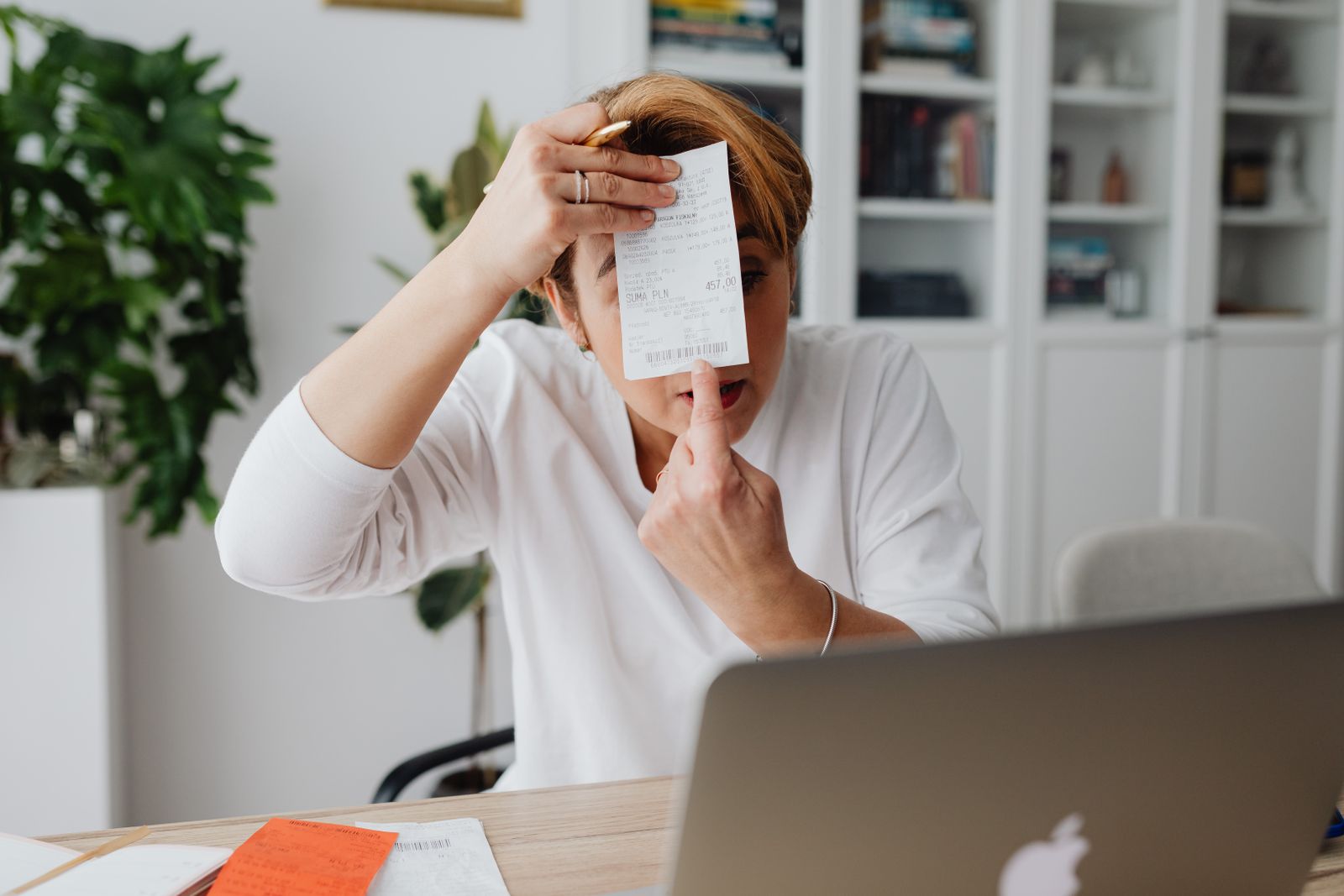 Person at a desk holding up a printed receipt next to a laptop
