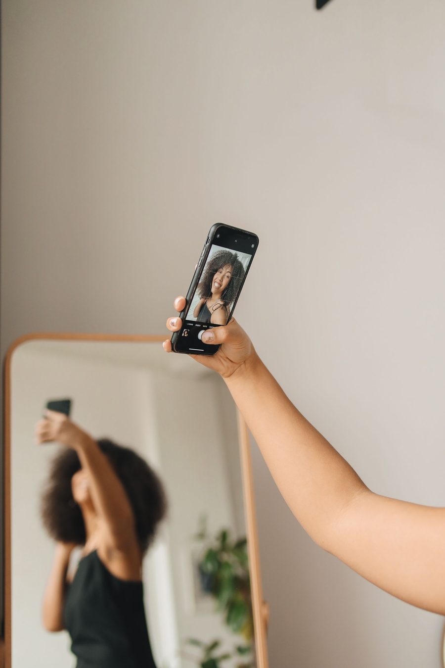 Woman taking a selfie in front of a mirror with a smartphone