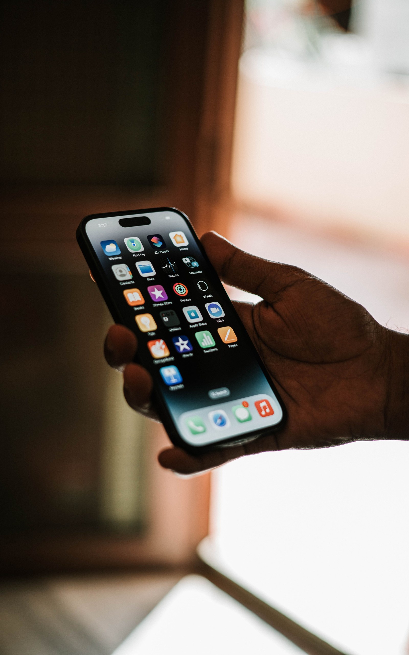 A hand holding a smartphone showing its home screen of app icons
