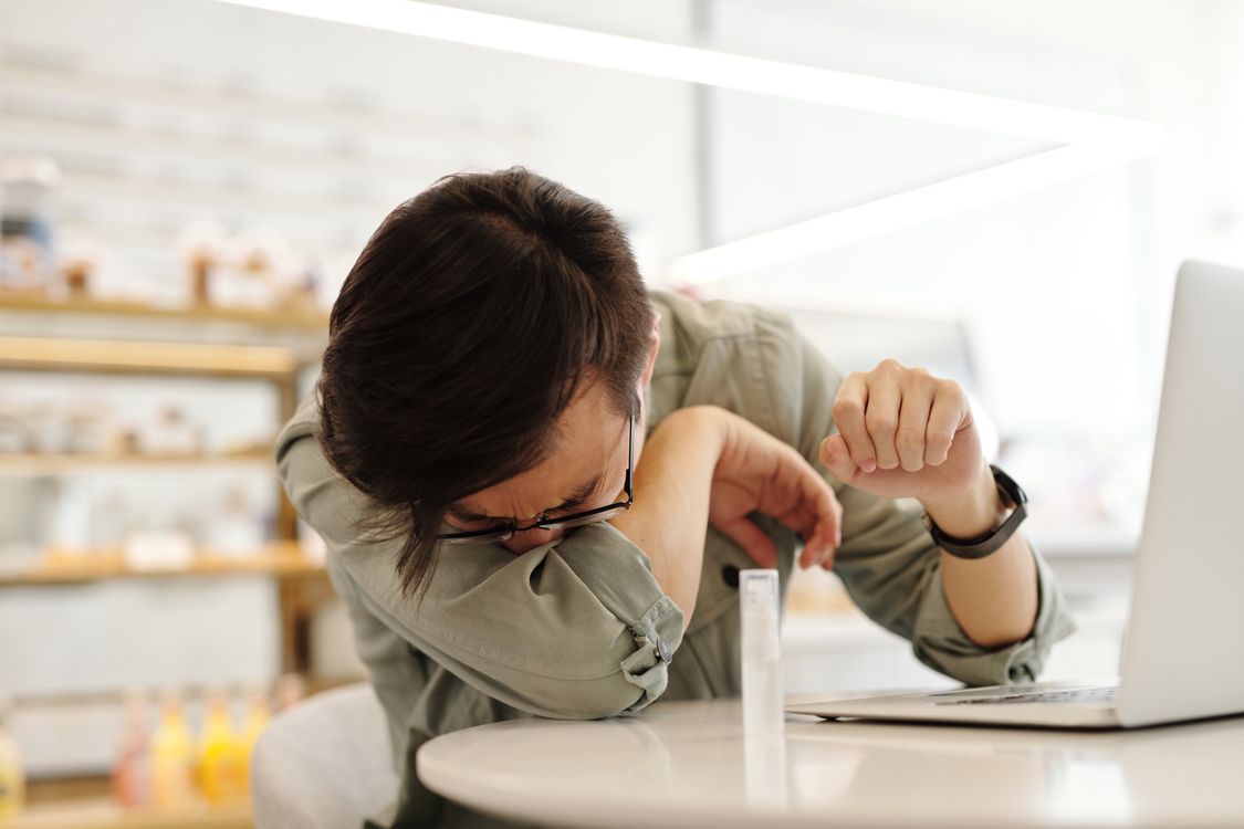 A person coughing into their elbow at a desk