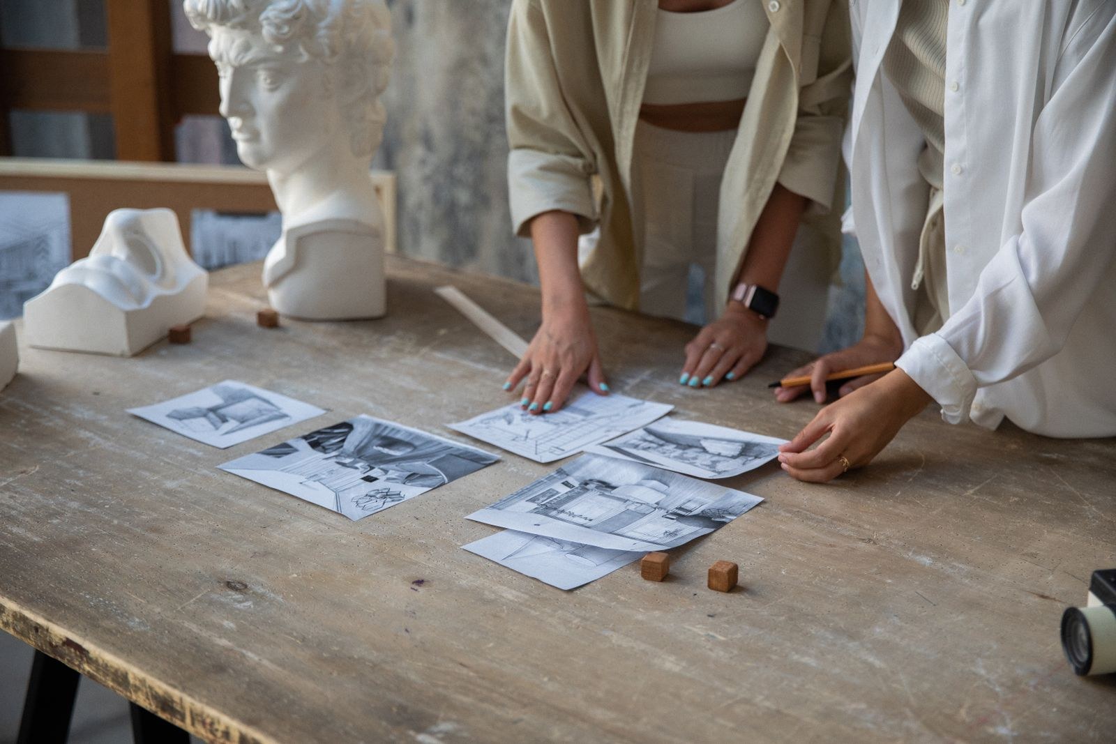Two people reviewing printed design images spread across a work table