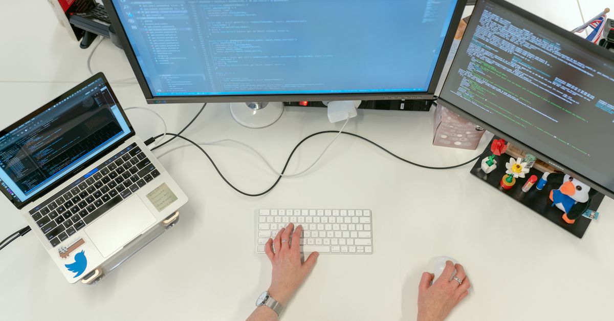 A software engineer working at a desk with dual monitors and a laptop
