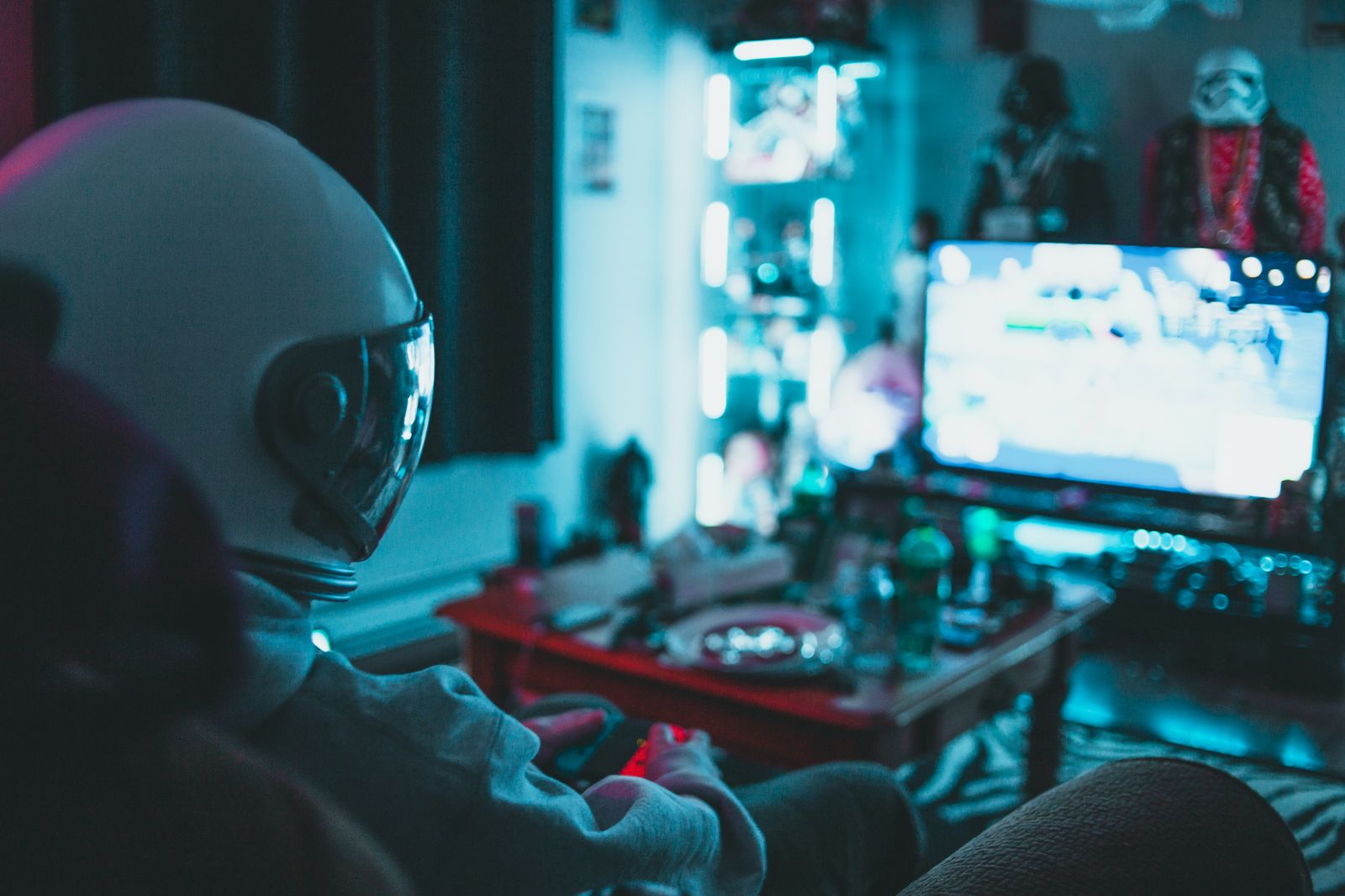 An astronaut figure playing a video game in a neon-lit dark room, monitor glowing