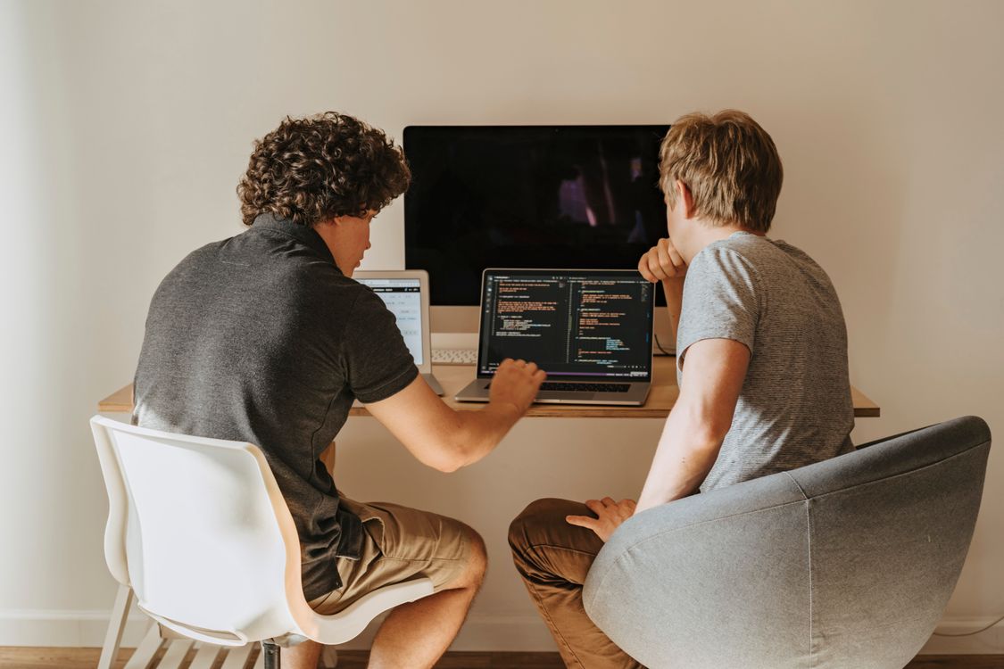 Two software developers discussing code over laptops; illustrative stock photo, not OpenAI or Anthropic employees