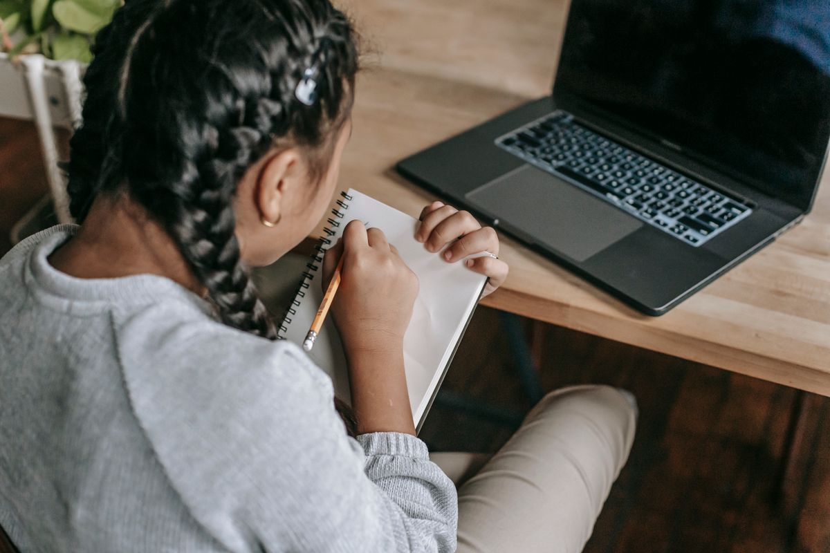 A student writing notes in a notebook beside a laptop