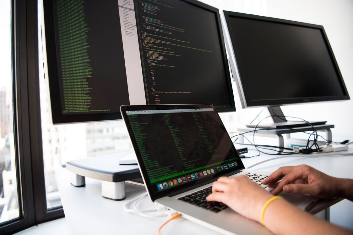 A developer writing code on a laptop in front of multiple monitors